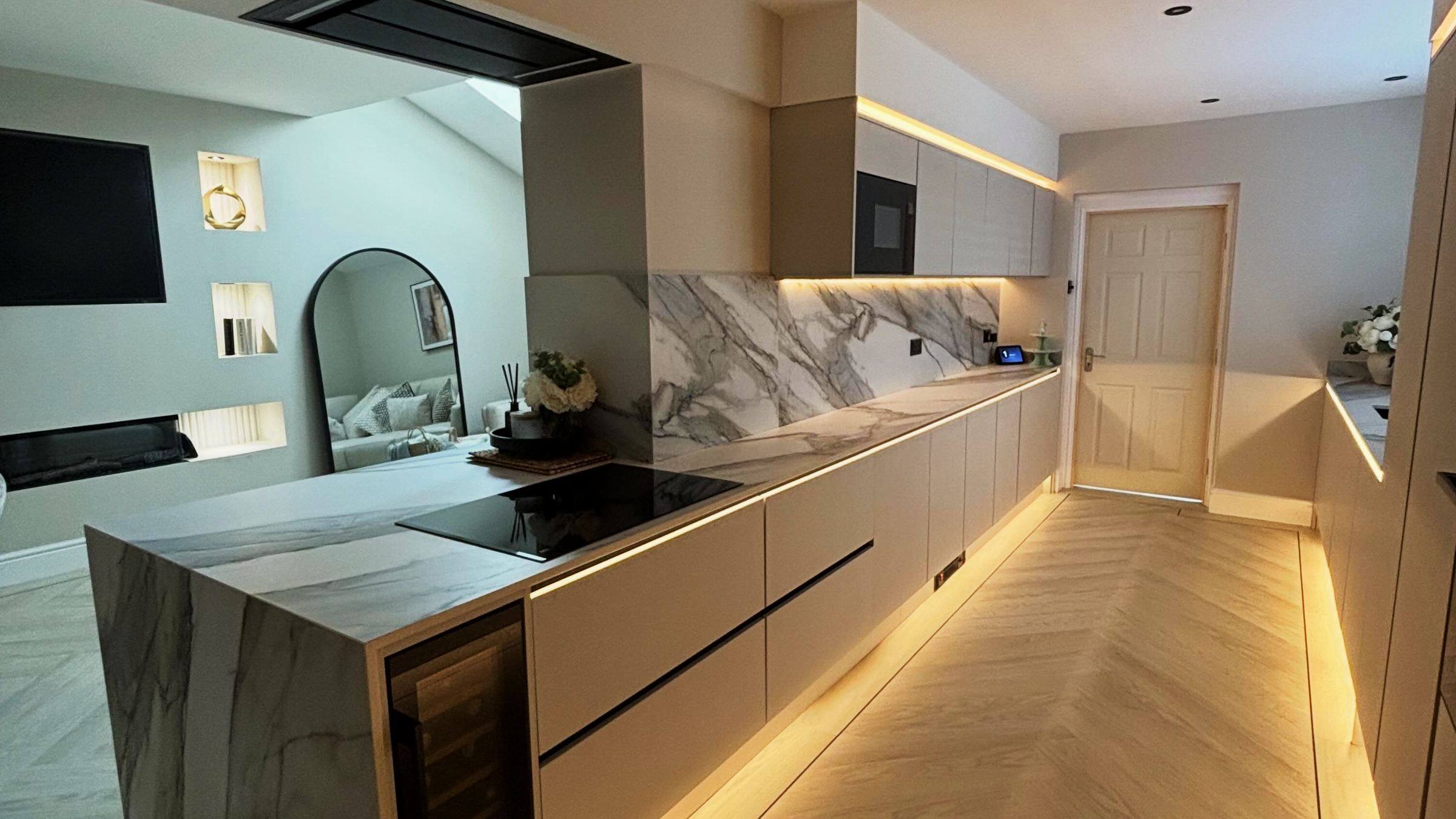 Taupe grey handleless kitchen with a porcelain worktop, a matching dining table and soft LED light under the plinth