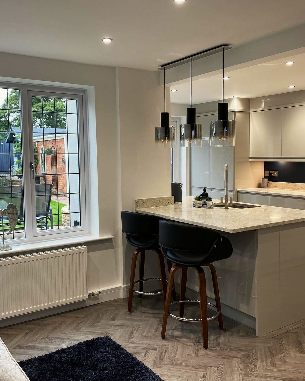 Open-plan gloss handleless kitchen with a quartz worktop, herringbone floor and French doors