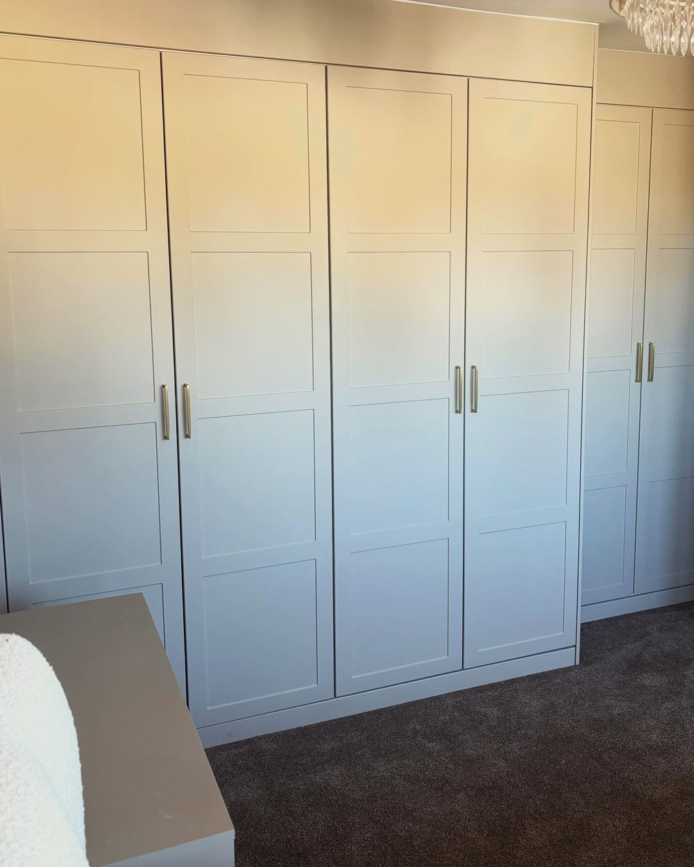 Taupe four-panel shaker wardrobes with reduced-depth units beside the bedroom door